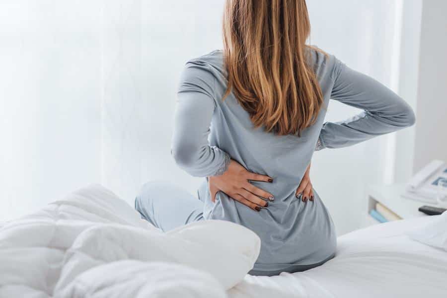 Woman-holding-back-stretching-morning Woman with back pain stretching in bed after waking up