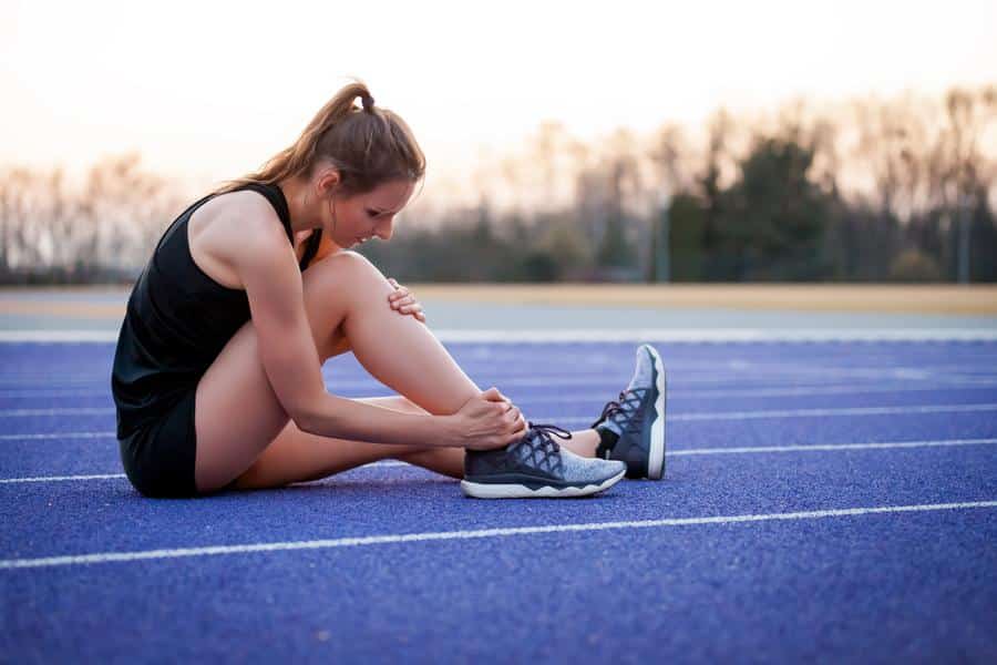 Woman-running-sports-injury Woman on track holding knee and ankle